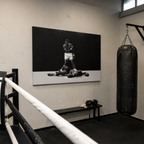 Ασπρόμαυρος πίνακας του Muhammad Ali σε γυμναστήριο πυγμαχίας με ρινγκ και σάκο του μποξ.
