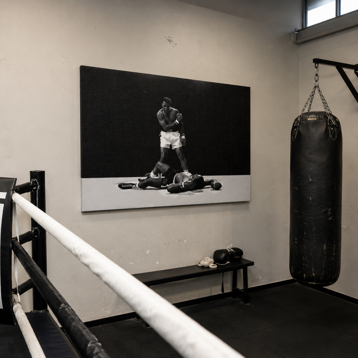 Ασπρόμαυρος πίνακας του Muhammad Ali σε γυμναστήριο πυγμαχίας με ρινγκ και σάκο του μποξ.
